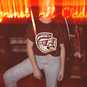 Woman sitting with mascot t shirt on at night with neon near camera